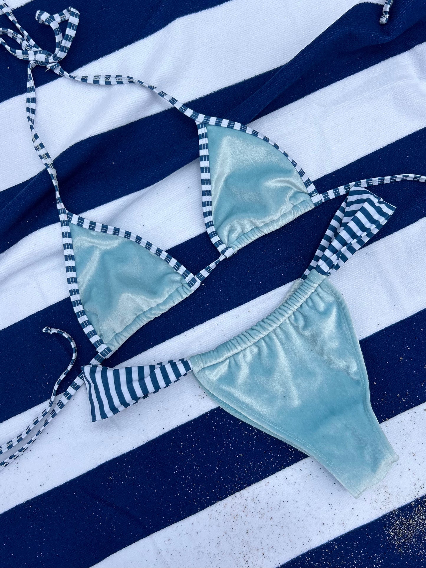 Light blue bikini set with striped straps on a blue and white striped background