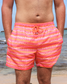 Person wearing pink and orange striped swim shorts on a beach.