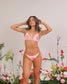 Woman wearing a pink floral bikini standing among flowers with a neutral background